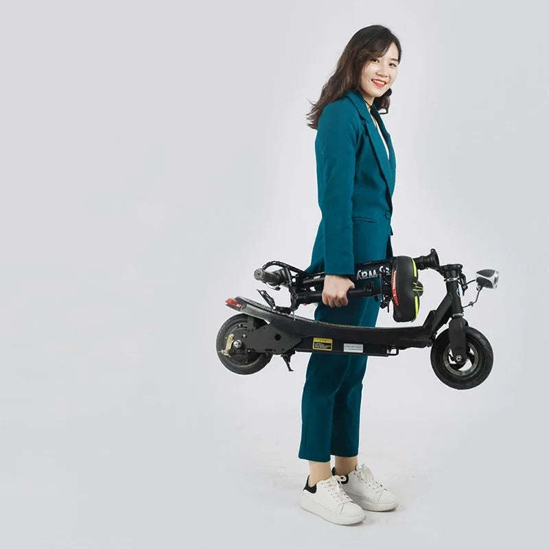 Woman in teal suit and white sneakers holding folded black electric scooter, minimalist background
