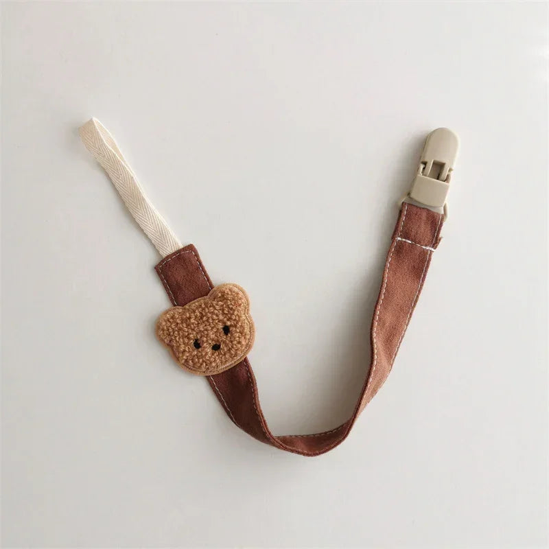 Brown fabric pacifier clip with plush bear face and beige plastic clasp, cute baby accessory