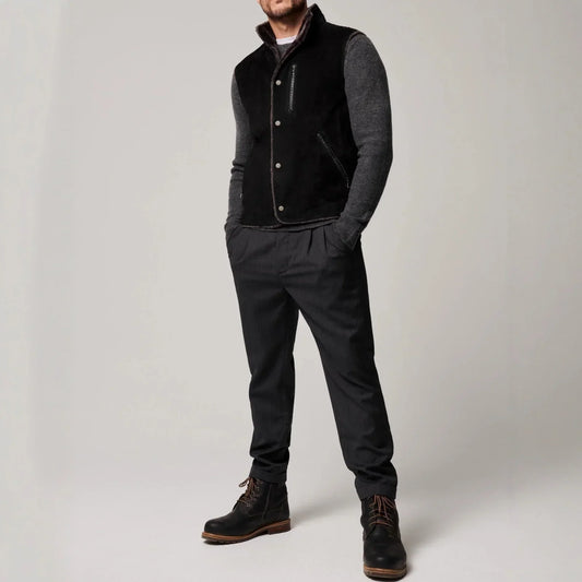 Man wearing a black suede vest, grey knit sleeves, dark tapered pants, and black boots.