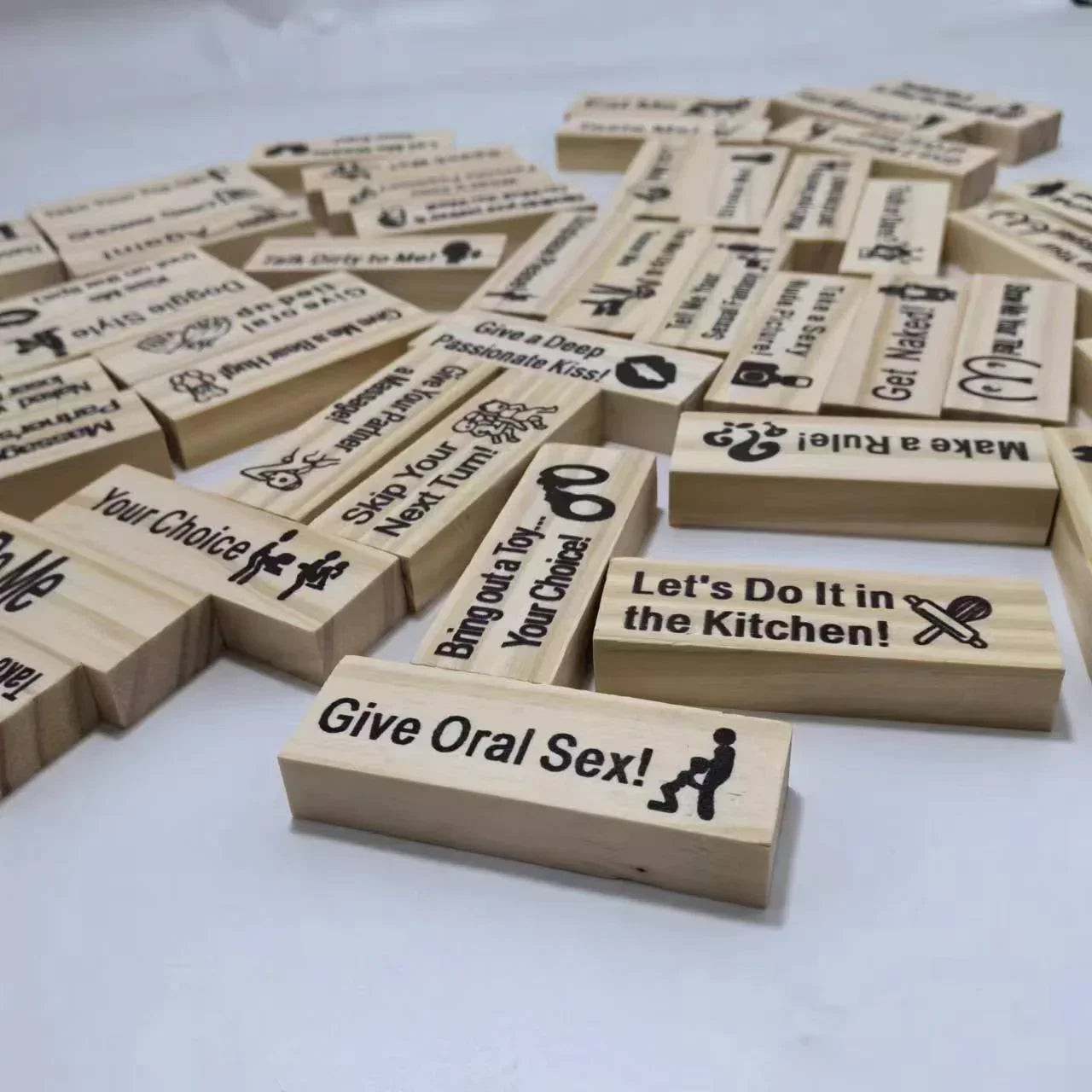 Image shows wooden blocks with adult-themed instructions printed on them, scattered on a table.
