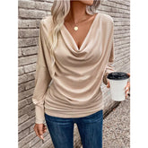 Woman wearing beige draped long sleeve top with relaxed fit and blue skinny jeans