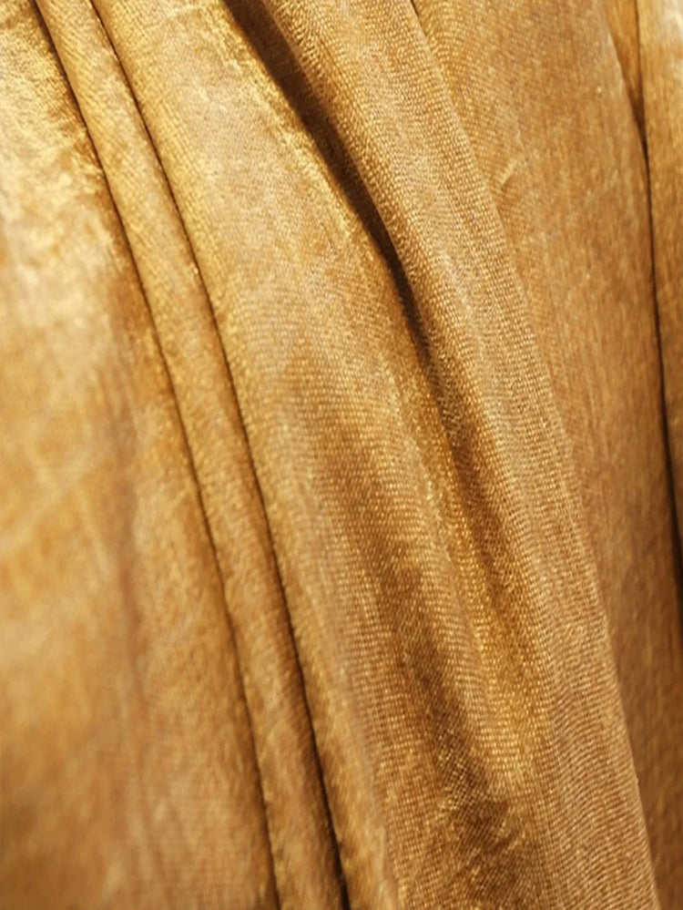 Close-up of gold velvet fabric with soft folds, highlighting textured, luxurious material