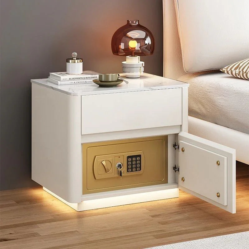 Modern white nightstand with marble top and built-in gold safe, positioned beside a bed.