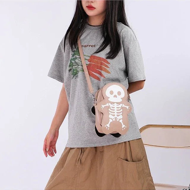 Woman wearing a loose grey graphic t-shirt, tan skirt, and beige skeleton crossbody bag.