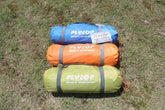 Three compact sleeping bags in blue, orange, and green nylon, laid on grass outdoors.