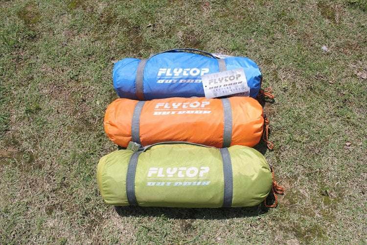 Three compact sleeping bags in blue, orange, and green nylon, laid on grass outdoors.