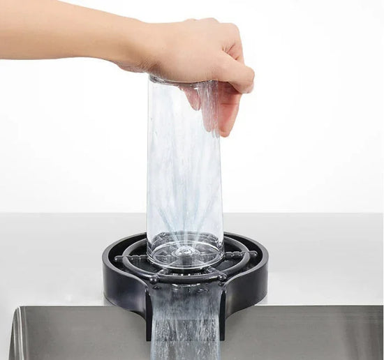 Hand rinsing clear glass cup on modern automatic kitchen cup washer with water spray