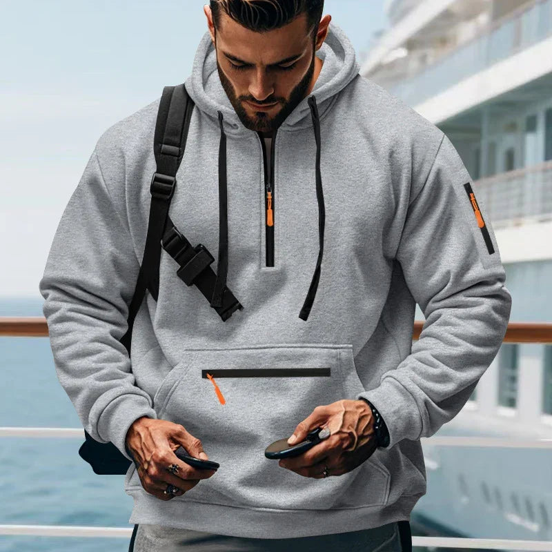 Man wearing a light grey streetwear hoodie with zippered pockets and relaxed fit outdoors