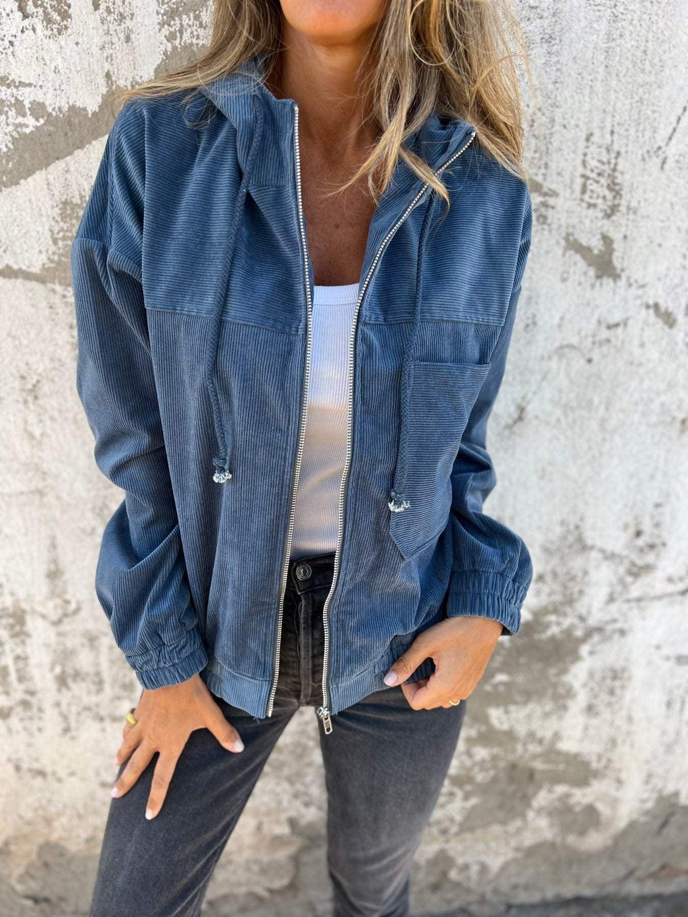 Woman wearing a loose-fit blue corduroy jacket with zipper, white tank top, and black jeans