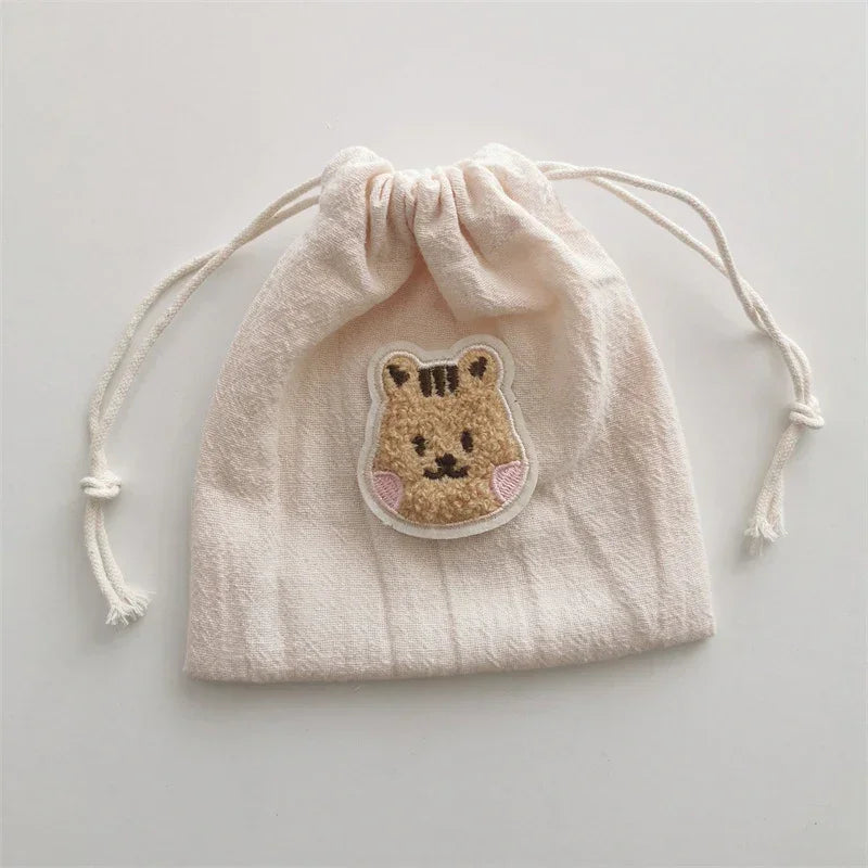 Beige cotton drawstring pouch with cute embroidered animal patch, soft textured fabric.