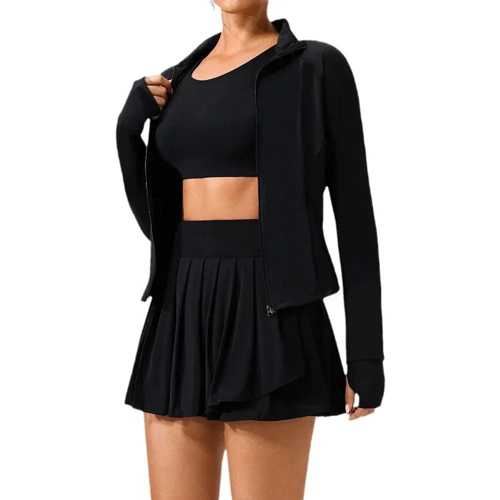 Woman wearing black crop top, pleated mini skirt, zip-up jacket, fitted activewear style
