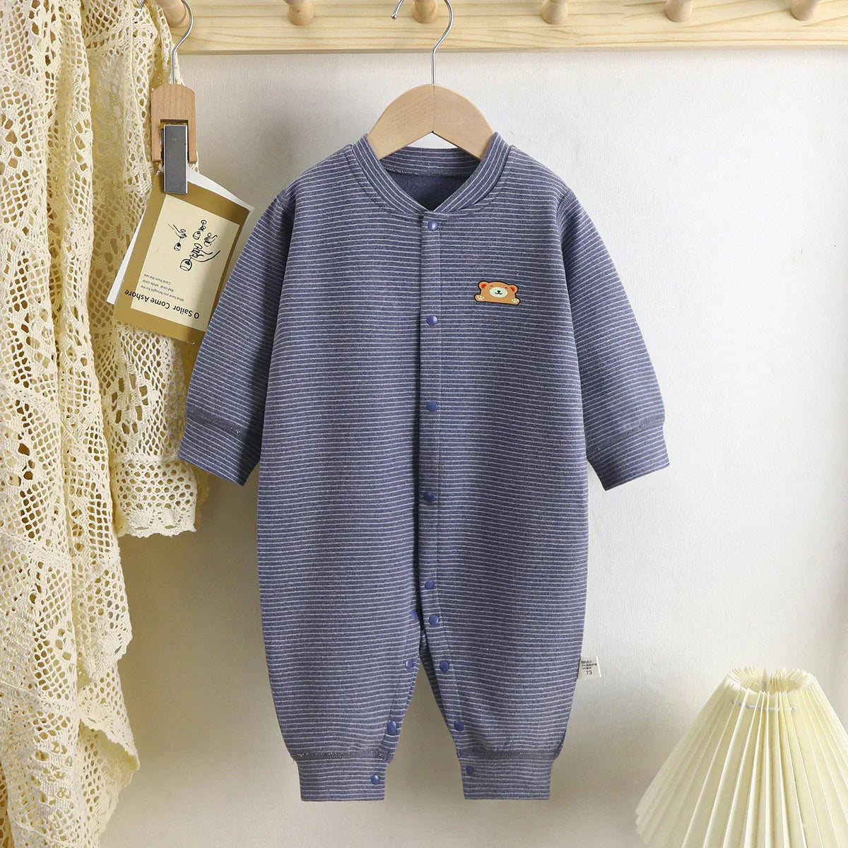 Blue striped baby romper with small bear patch, long sleeves, snap closure, cotton fabric