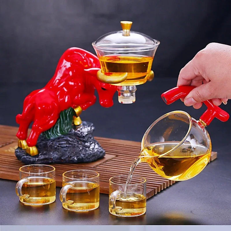 Modern glass teapot set with red bull-shaped base, pouring tea into clear glass cups.