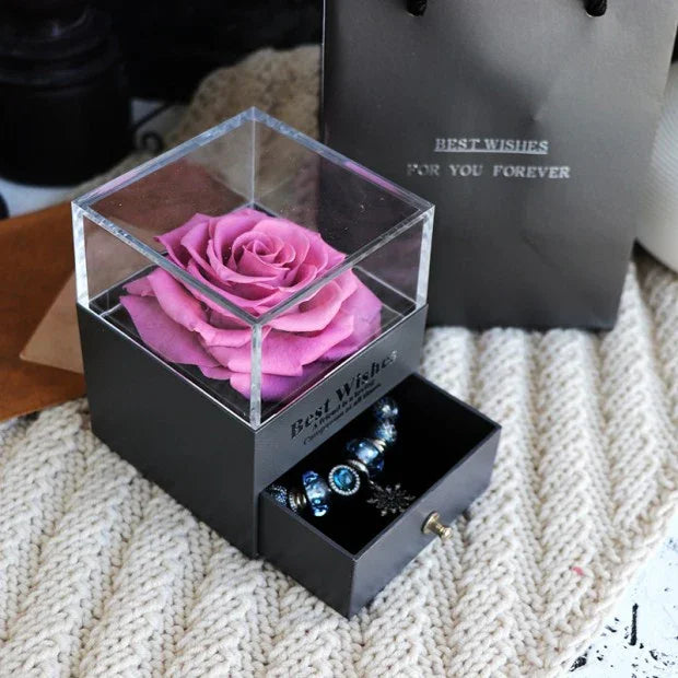 Black jewelry box with pink preserved rose in clear display and open drawer with blue beaded bracelet