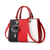 Colorblock handbag with red, black, and white panels, faux leather, gold hardware, and pompom charm