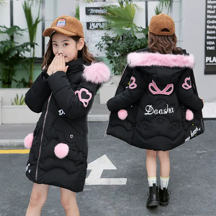 Girl wearing black puffer coat with pink faux fur trim, heart patches, and loose fit