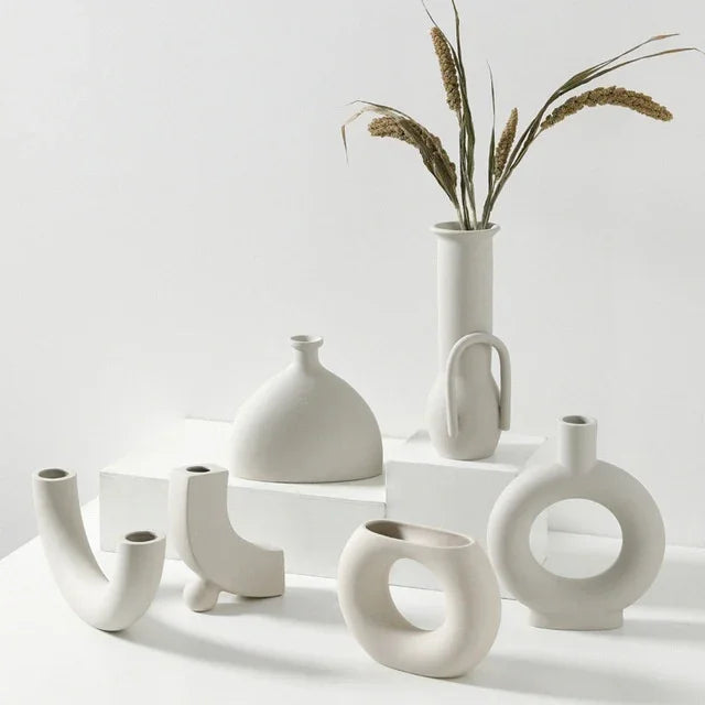 Minimalist white ceramic vases with unique geometric shapes on a white display, dried grass in tall vase.