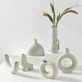 Minimalist white ceramic vases with unique geometric shapes on a white display, dried grass in tall vase.