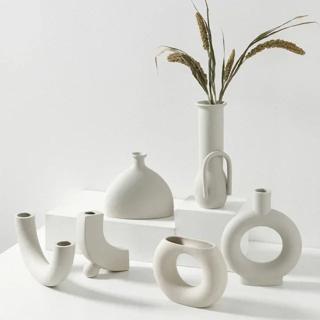 Minimalist white ceramic vases with unique geometric shapes on a white display, dried grass in tall vase.