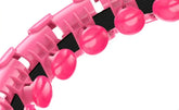 Closeup of a pink adjustable exercise hoop with textured massage nodes and black grip strip.