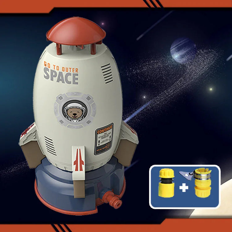 Toy rocket-shaped sprinkler in gray and red plastic with space-themed design and included yellow hose connectors