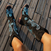 Black suede cowboy boots with blue floral embroidery, mid-calf fit, wooden deck background