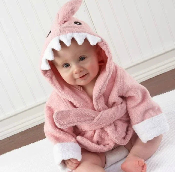 Baby in pink hooded shark robe, plush terry material, relaxed fit, sitting indoors