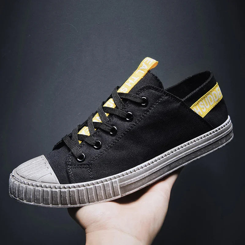 Black canvas low-top sneaker with yellow accent details and rubber sole, streetwear style