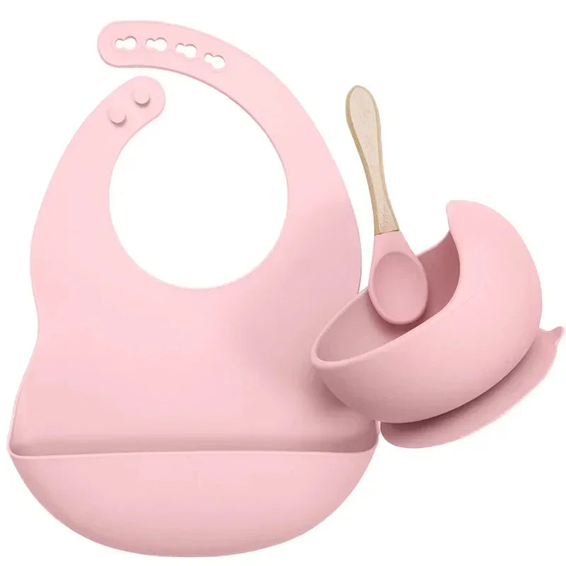 Pink silicone bib, suction bowl, and spoon set for babies or toddlers, modern design.