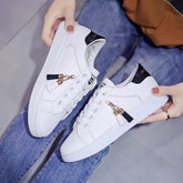 White low-top sneakers with black accents, gold tassel charms, and a slim fit design