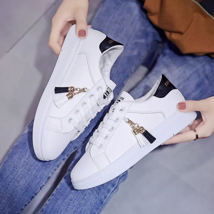 White low-top sneakers with black accents, gold tassel charms, and a slim fit design