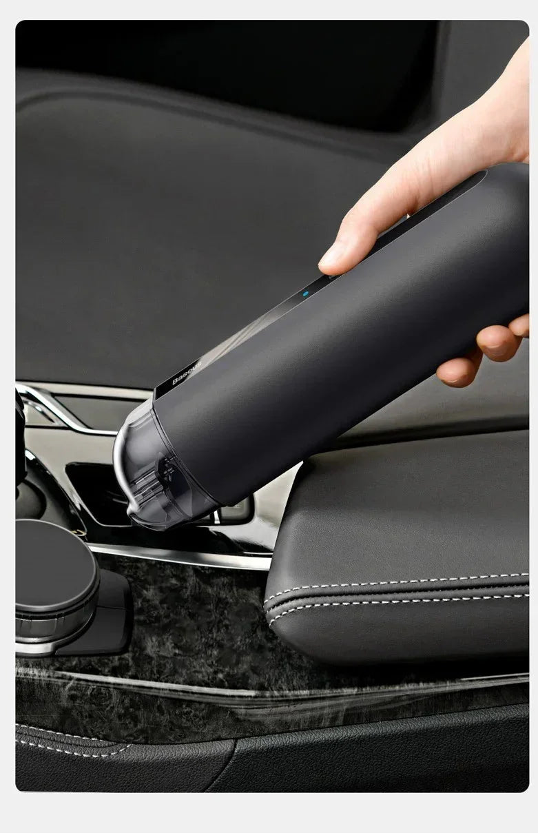 Hand using sleek black portable vacuum cleaner on car interior leather seat.
