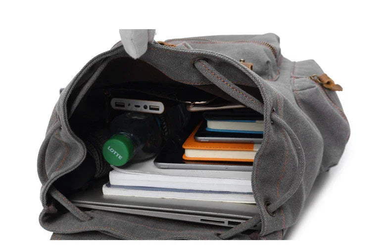 Open grey canvas backpack with laptop, notebooks, water bottle, and tech accessories inside