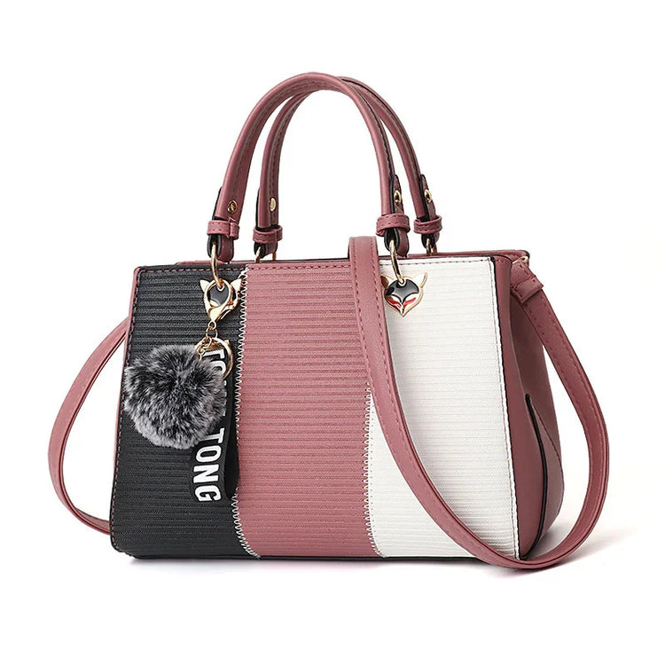 Color block handbag with pink, black, and white panels, textured faux leather, structured fit, top handles, and fluffy pom pom charm.
