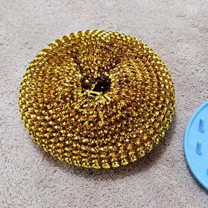 Metallic gold scrubber with textured surface on beige background, cleaning accessory