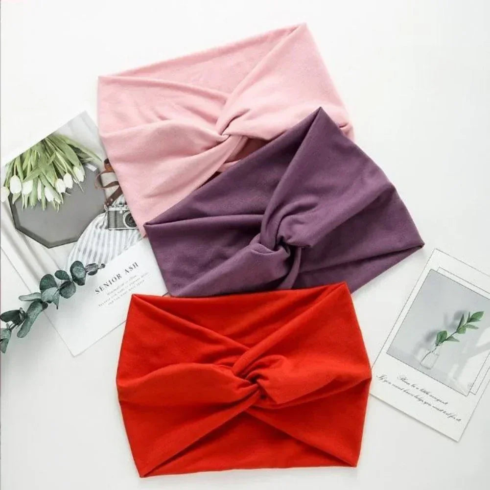 Three twisted knot headbands in pink, purple, and red soft fabric, laid flat on white surface.