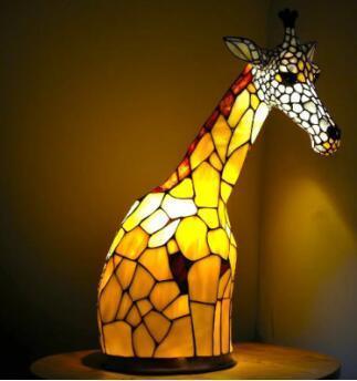 Stained glass giraffe lamp with warm yellow and brown tones, illuminated in a dark room