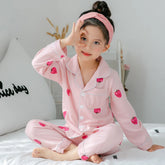Child in pink cotton pajamas with red apple print, relaxed fit, sitting on a bed