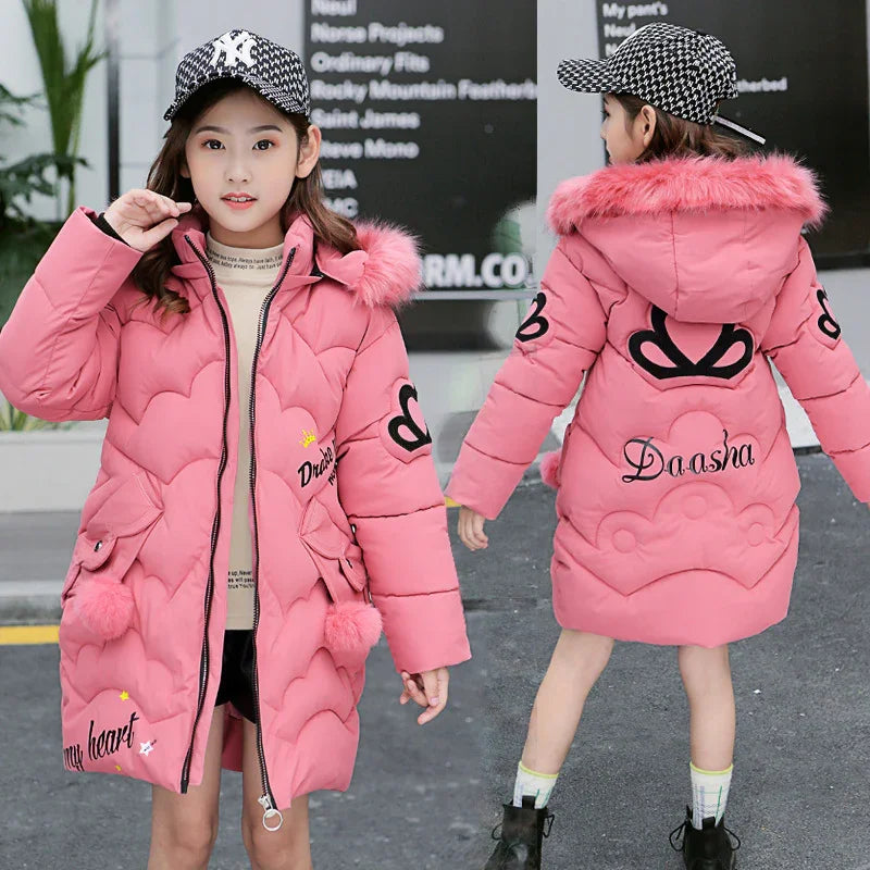 Girl wearing pink padded winter coat with faux fur hood, heart patches, and relaxed fit