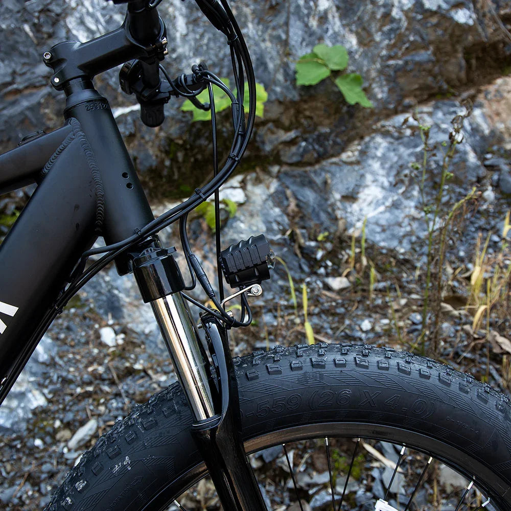 Close-up of matte black mountain bike front tire, thick tread, and metal suspension fork outdoors