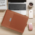 Brown leather laptop sleeve with slim fit on wooden desk beside laptop, coffee, and phone.