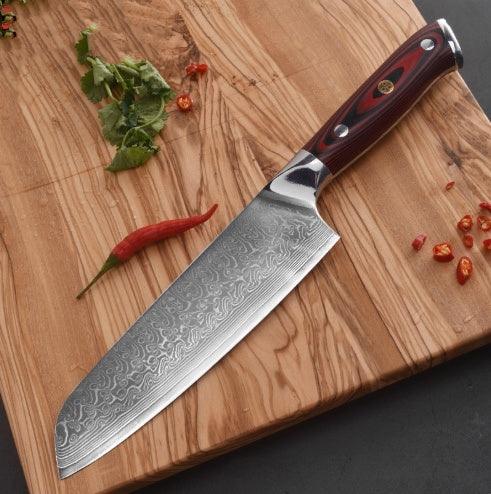 Damascus steel chef knife with red wood handle on wooden cutting board with chili and herbs