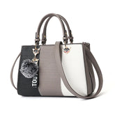 Colorblock satchel handbag in black, taupe, and white faux leather with double handles and pom pom charm