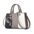Colorblock faux leather handbag with gray, black, and white panels, top handles, and pom pom charm