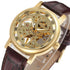 Gold skeleton watch with Roman numerals, brown leather strap, and visible mechanical movement