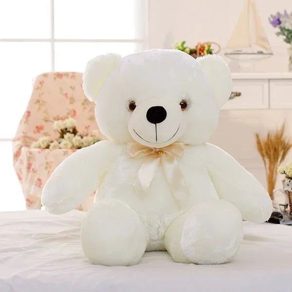 Plush white teddy bear with a ribbon bow, soft fabric, sitting on a bed in a cozy room.