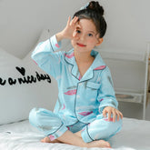 Child wearing light blue feather print pajamas with black piping, sitting on bed
