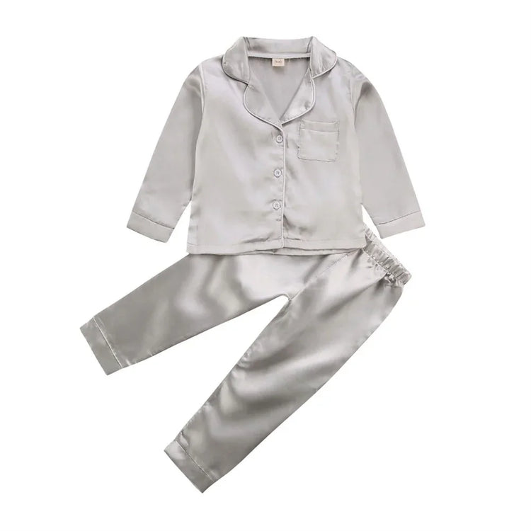 Silver satin pajama set with long sleeves, button front, chest pocket, and relaxed fit pants