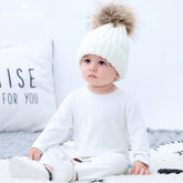 Baby in white knit pom pom beanie and white long-sleeve outfit, relaxed fit, cozy style