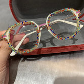 White square-frame glasses with colorful rhinestone accents, held in a velvet case.
